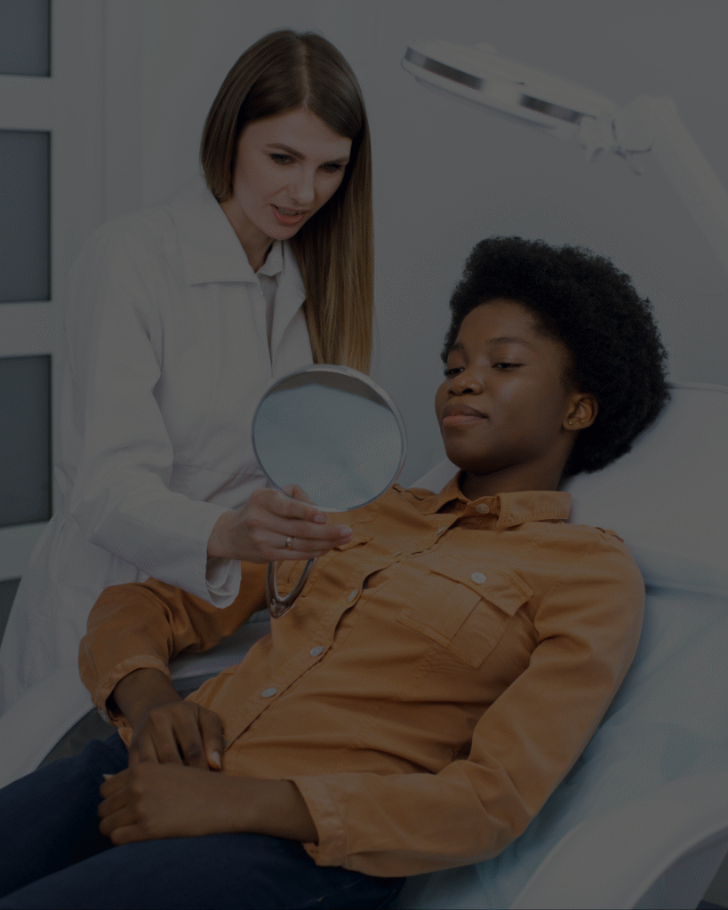 Image d'une esthéticienne montrant la peau de sa client à l'aide d'un miroir qu'elle tient dans sa main droite.