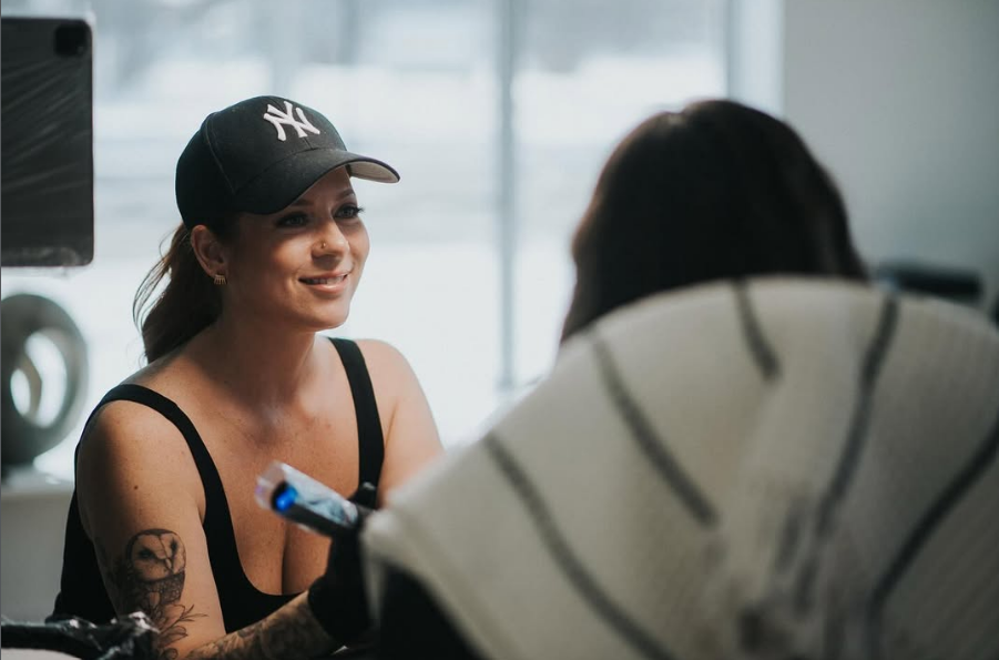 Tatoueuse ayant une machine à tattoo dans sa main droite et souriant.